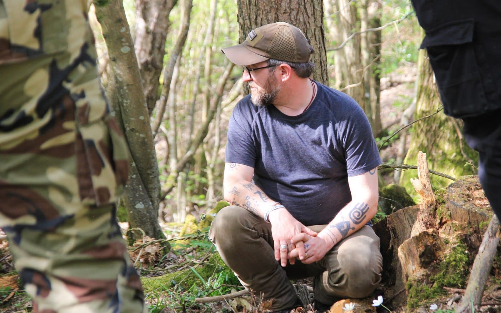 Sam crouching in the woods among a small group, at home in his working setting.